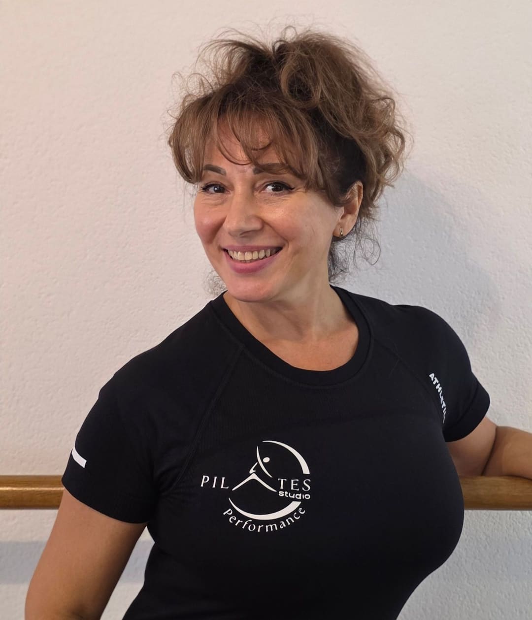 Nasmejana osoba u majici sa logom studija oslonjena na šipku
