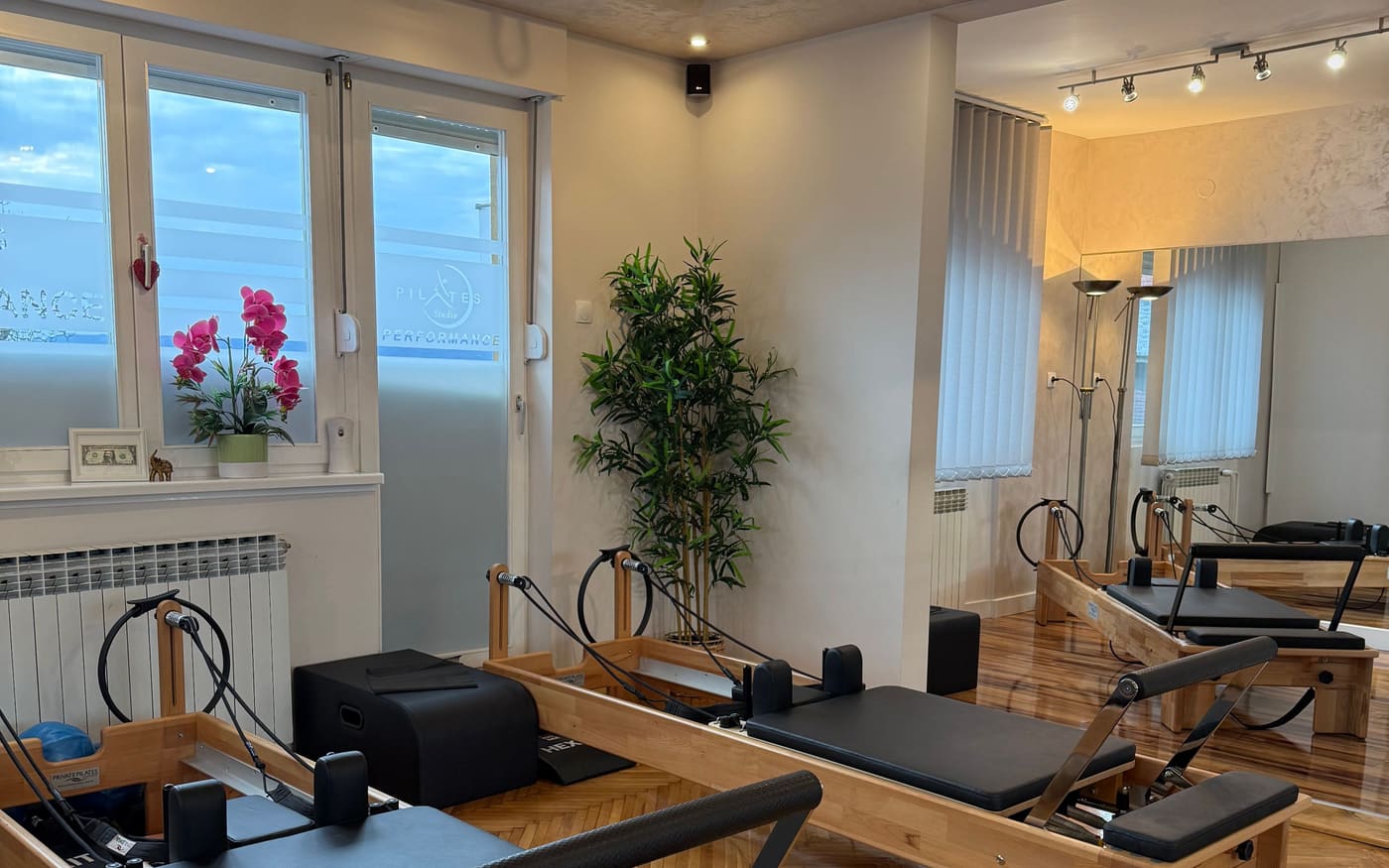 Studio sa drvenim reformerima, prozorom sa logom studija i ogledalom